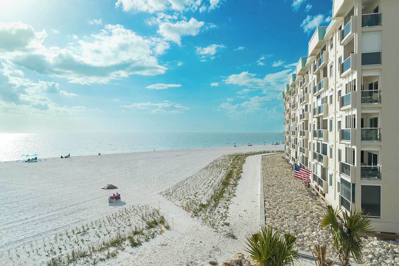 A beachfront hotel with a sandy beach, ocean view, and an American flag.