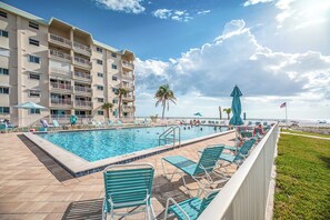 Ein Hotelpoolbereich mit freiem Blick auf das Meer, ein Gebäude mit Balkonen und ein umzäunter Pool.
