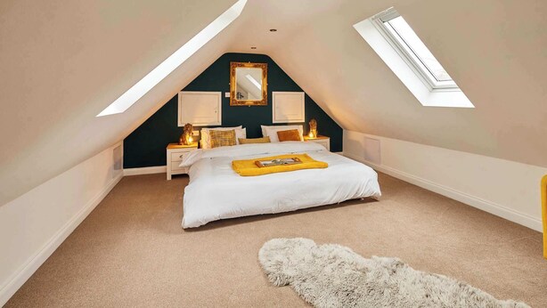 Une chambre avec un plafond en pente, un lit, une table de chevet, un miroir et une fenêtre.
