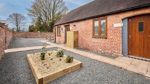 Un bâtiment en briques avec une porte en bois, une fenêtre et un petit jardin agrémenté de gravier et de plantes.
