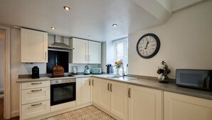 Une cuisine moderne avec des meubles blancs, un four encastré, une machine à café, une bouilloire et une horloge murale.