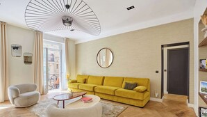 Una sala de estar moderna con sofá, sillón, y mesa de centro, un ventilador grande y una puerta.