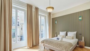 Un dormitorio con cama, cortinas, una lámpara colgante, suelo de madera y ventana con vistas.