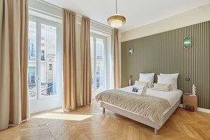 Une chambre à coucher avec un lit, des rideaux, une lampe suspendue, un plancher en bois et une fenêtre donnant sur un paysage agréable.