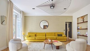 Una sala de estar moderna con un sofá amarillo, dos sillones blancos, una mesa de centro redonda y un espejo grande en la pared.