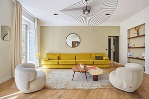 Un salon moderne avec un canapé jaune, deux fauteuils blancs, une table basse ronde et un grand miroir au mur.