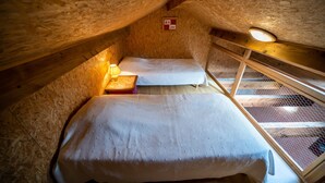 A small, cozy attic bedroom with a single bed, a nightstand, and a window with a mesh screen.