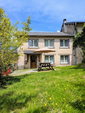 A two-story house with a front patio, a wooden table, and a bench.