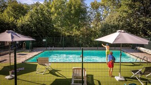 A swimming pool with a fence, lounge chairs, and umbrellas.