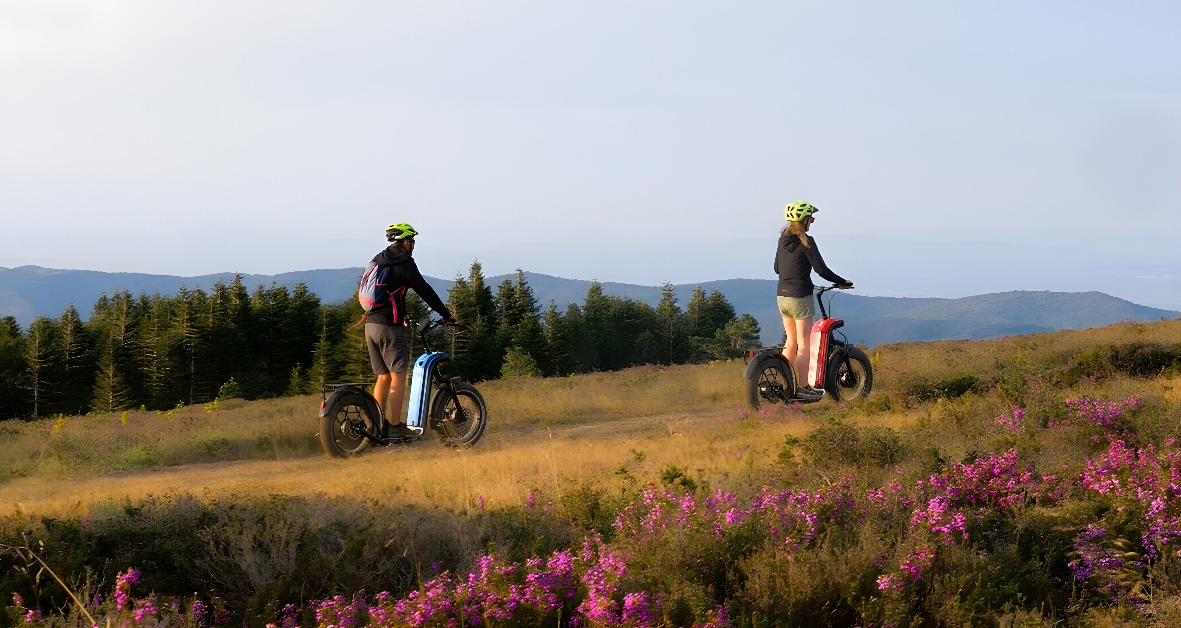 Twee personen op elektrische fietsen in een natuurlijke omgeving, met bergen op de achtergrond.