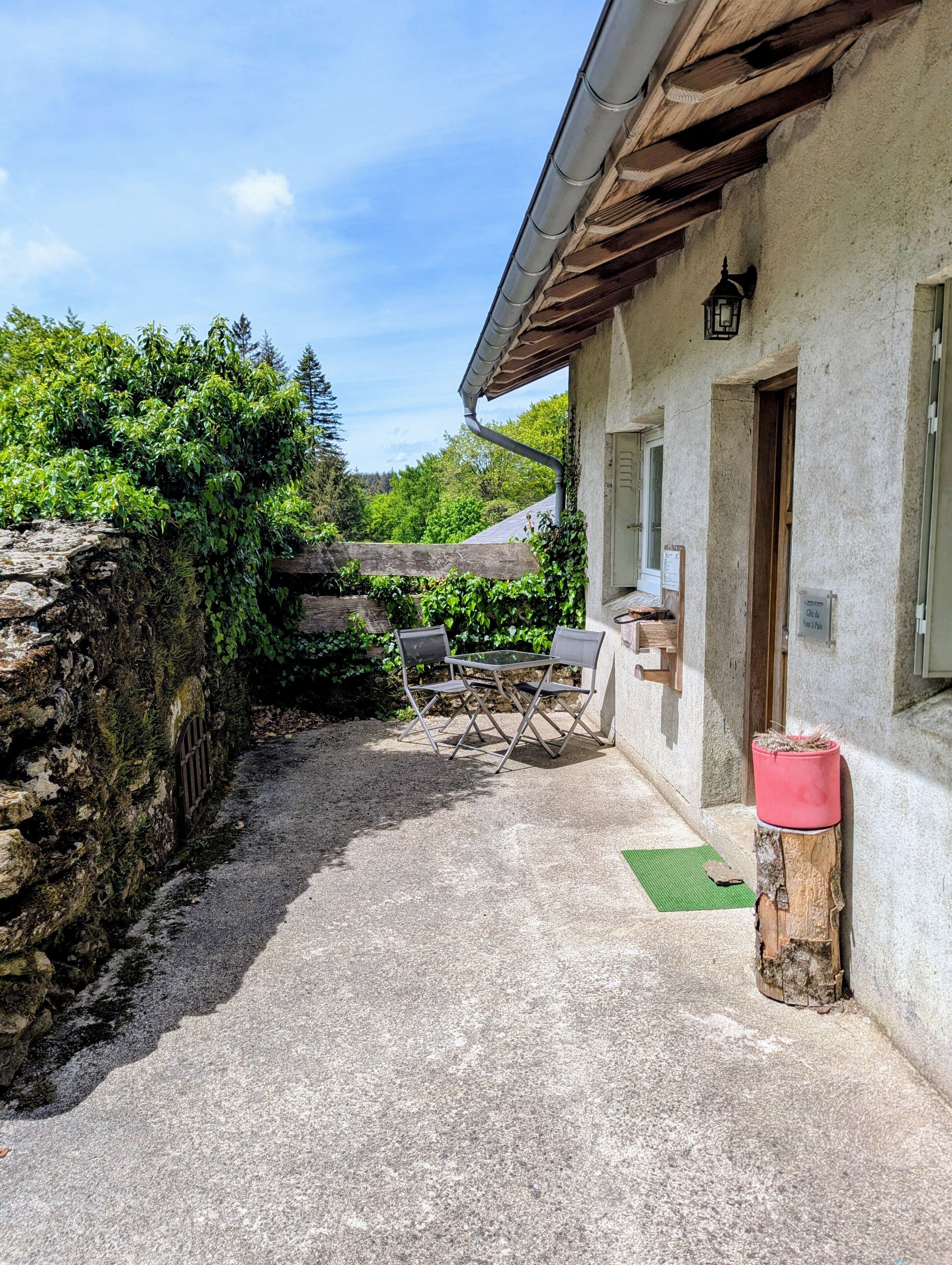 Un mur de pierre, un chemin de gravier, une table en métal avec des chaises, une porte en bois et une lanterne.
