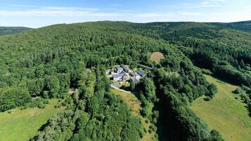 Luchtbeeld van een woongebied met huizen, omringd door dicht bos, een tennisbaan en glooiende heuvels.