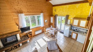 A wooden cabin with a dining area, kitchen, and a fireplace. - Cool Nature Retreat with Pool in the Heart of the Forest (Le Soulié)