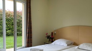A hotel room with two beds, a sliding glass door to the outside, and a small bedside table with a vase of flowers. - French country home II (Les Forges)