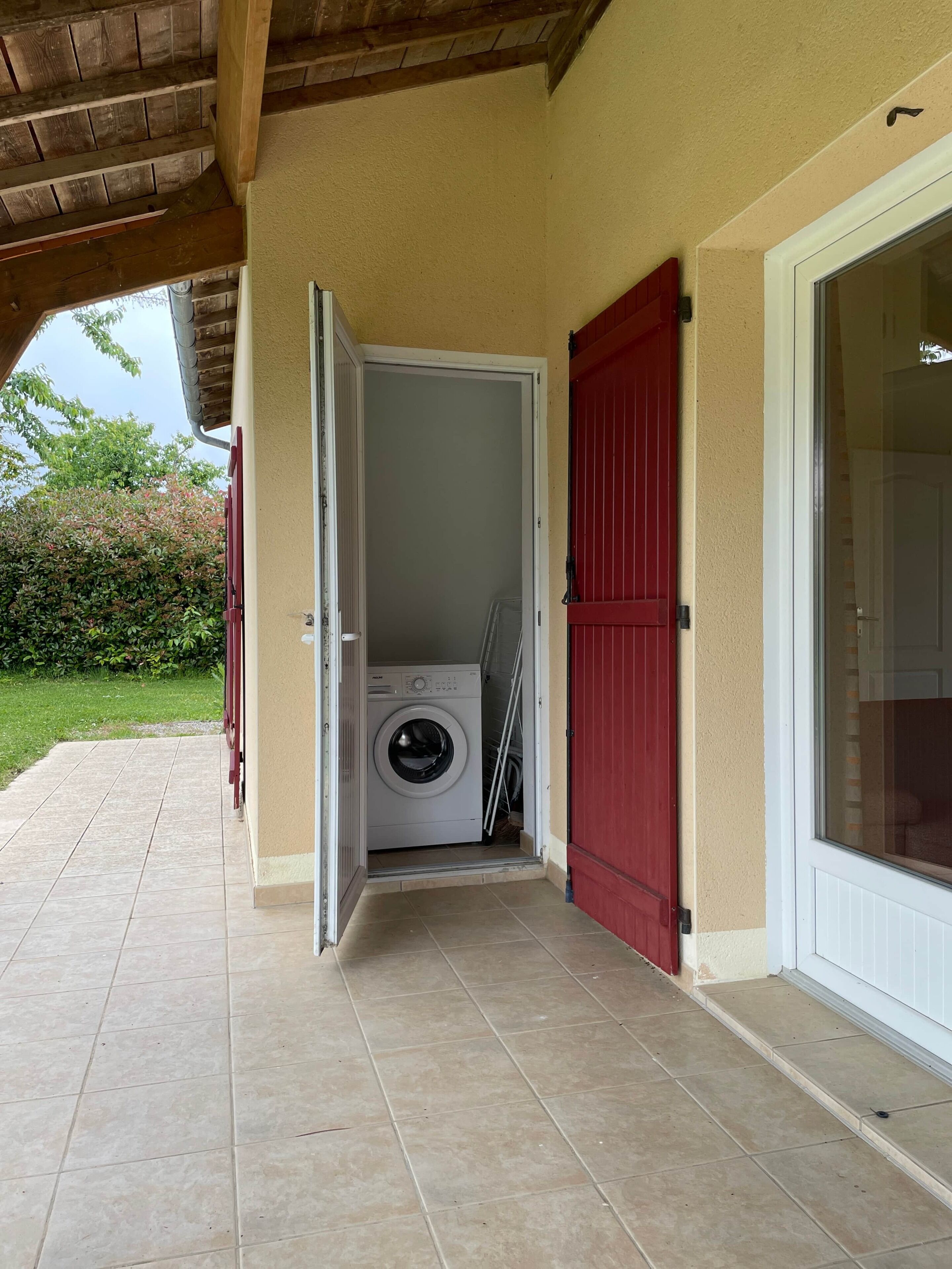 A laundry room with a washing machine, a red door, and a tiled floor.