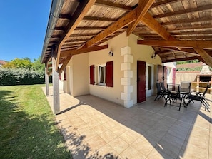 A covered patio area with a tiled floor, a wooden ceiling, and a seating arrangement.