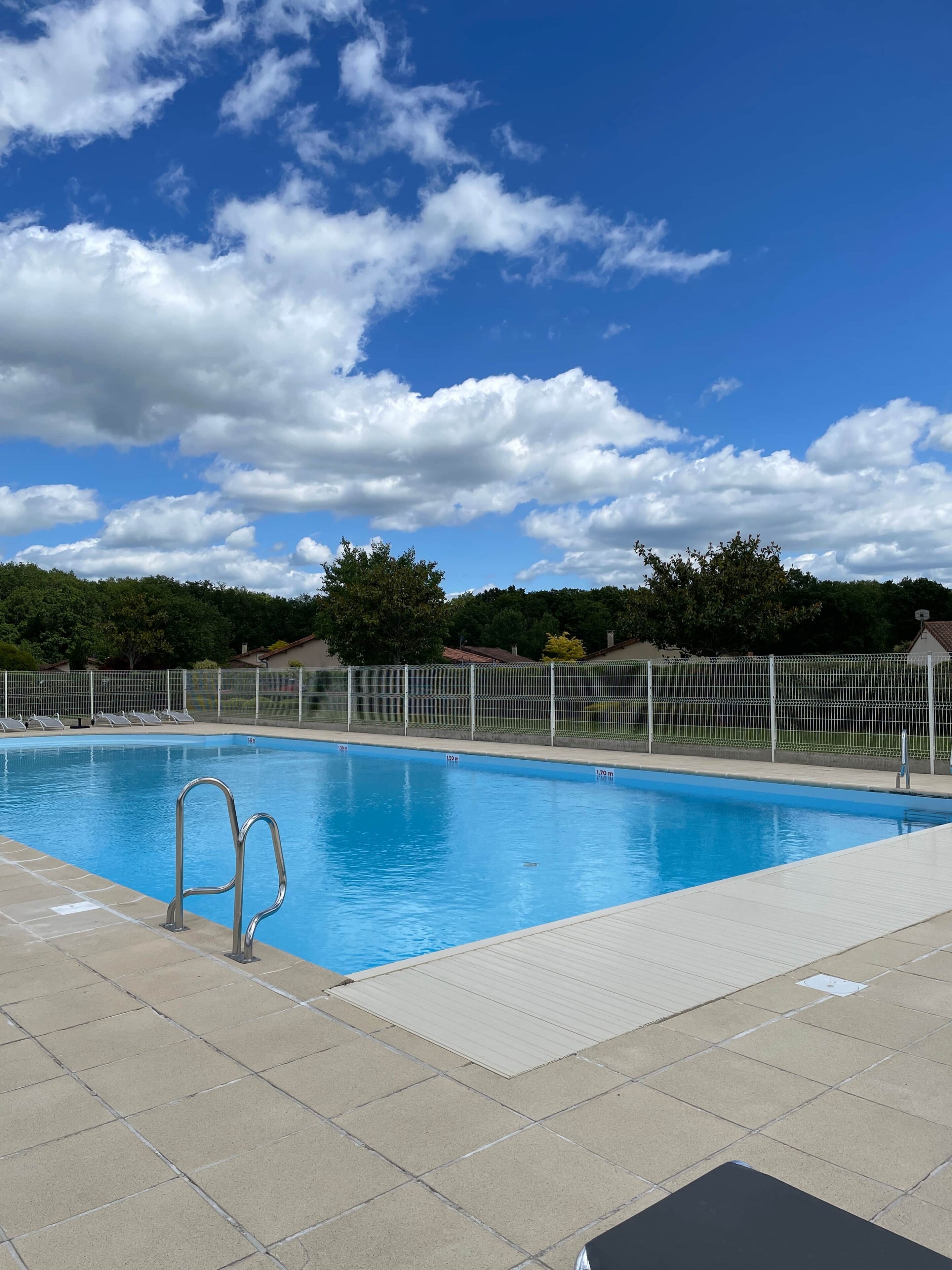 A swimming pool with a metal ladder, surrounded by a fence, and a clear blue sky above.