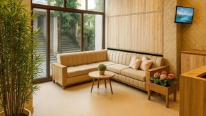 A modern living room with a beige sofa, a small round table, a potted plant, and a TV mounted on the wall. - Rosewood By Zenvana (Dehradun)