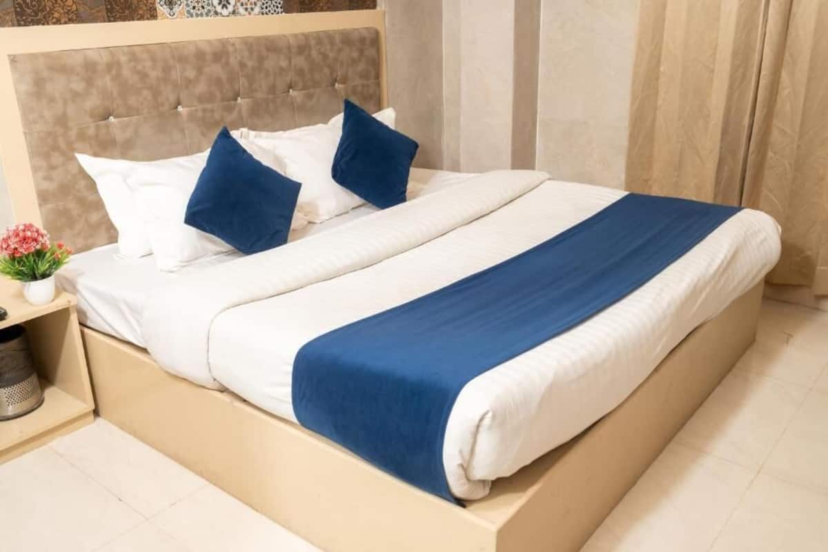 A neatly made bed with a headboard, white and blue bedding, and a small bedside table with a flower vase.