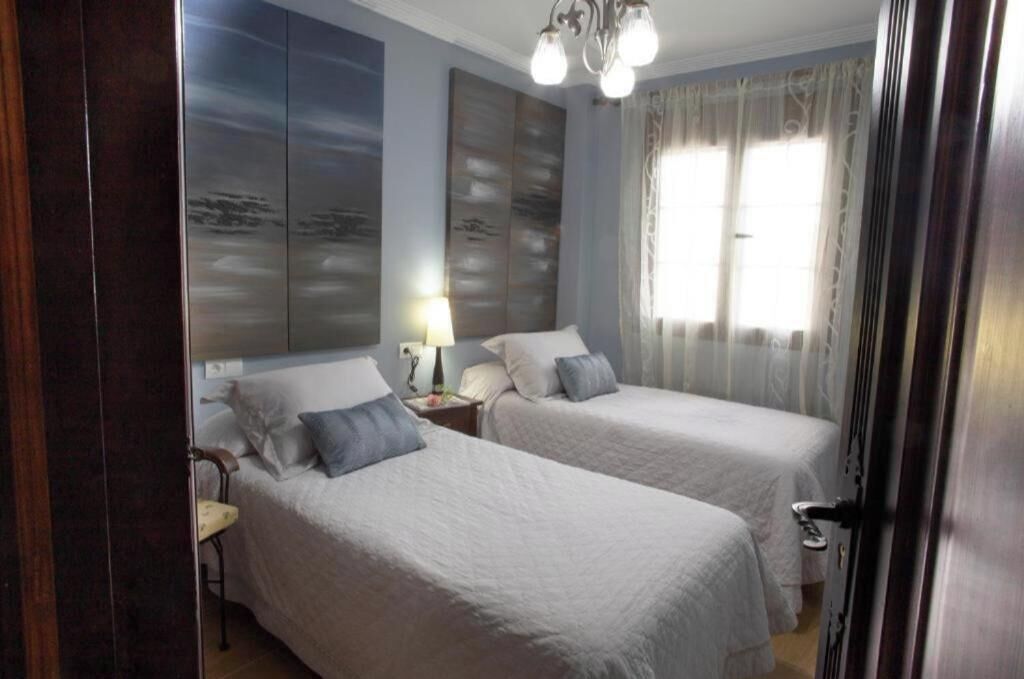 Une chambre avec deux lits, une table de chevet, une lampe et une grande fenêtre avec des rideaux.