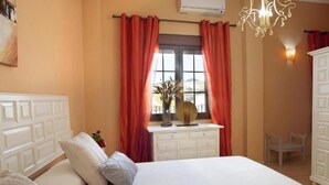 Un dormitorio con cama, cómoda, ventana con cortinas, candelabro y aire acondicionado de pared.