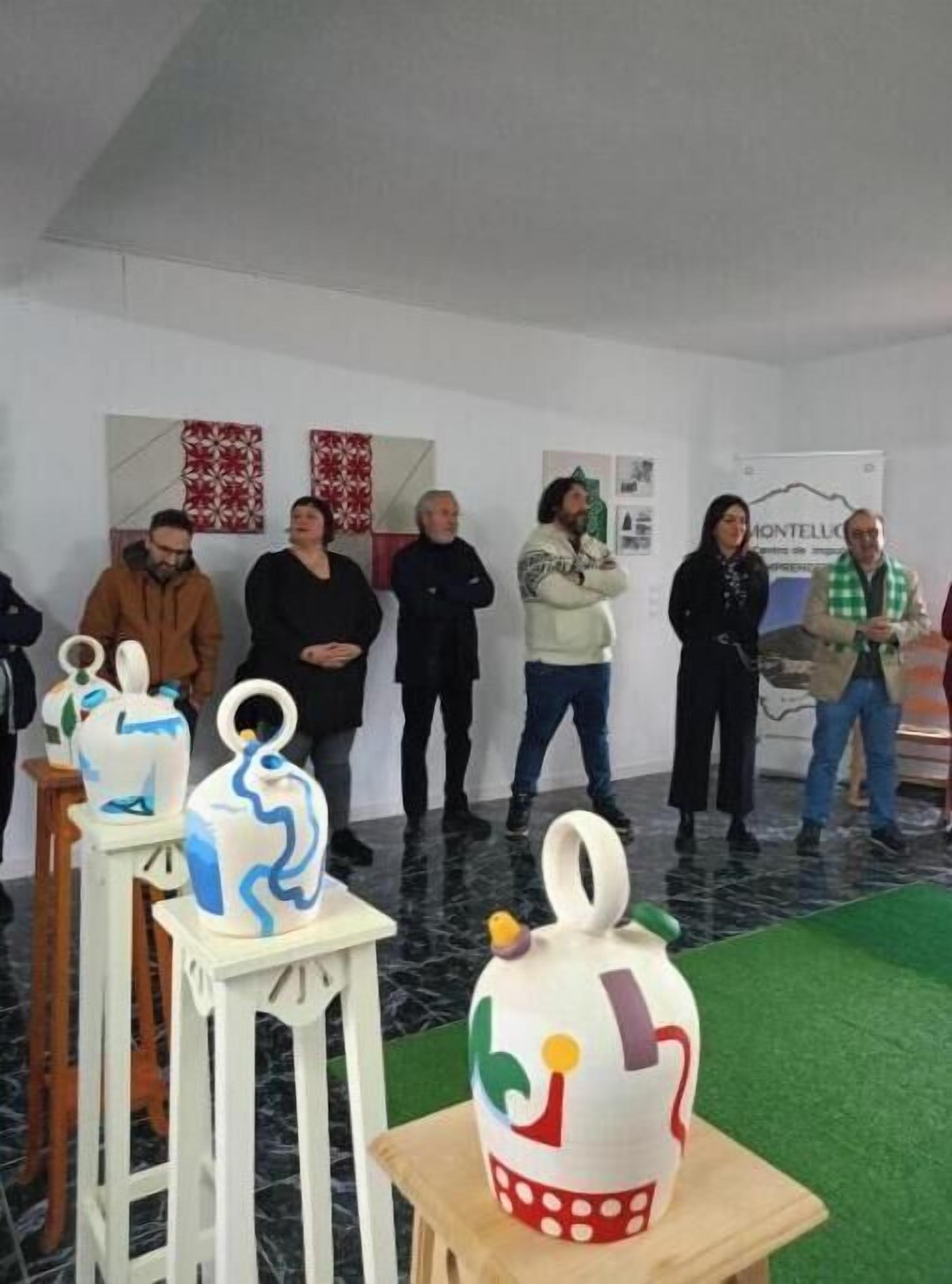 Un grupo de personas en una habitación con paredes blancas y alfombra verde, de pie frente a una exhibición de jarrones de cerámica.