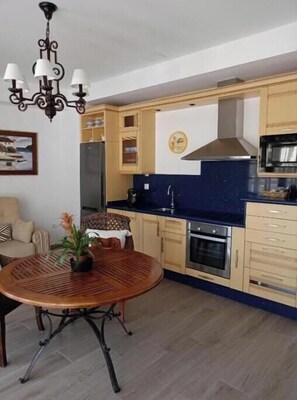 A kitchen with wooden cabinets, a stove, a microwave, and a dining area with a round table. - Villa Cultural MONTELUCÍA - Disconnection and Rural Inspiration (up to 20 people)  (Montecorto)