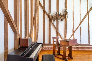 Ein Zimmer mit freiliegenden Holzbalken, einem Klavier, einem Holzstuhl und einem kleinen Tisch.