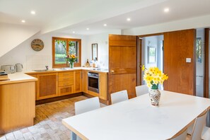 Eine moderne Küche mit Holzschränken, einer weißen Arbeitsplatte, einem Esstisch mit Stühlen und einem Blumenstrauß mit gelben Blumen.