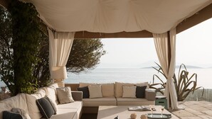 Un saló davant del mar amb un sofà, una taula amb begudes i un ordinador portàtil.