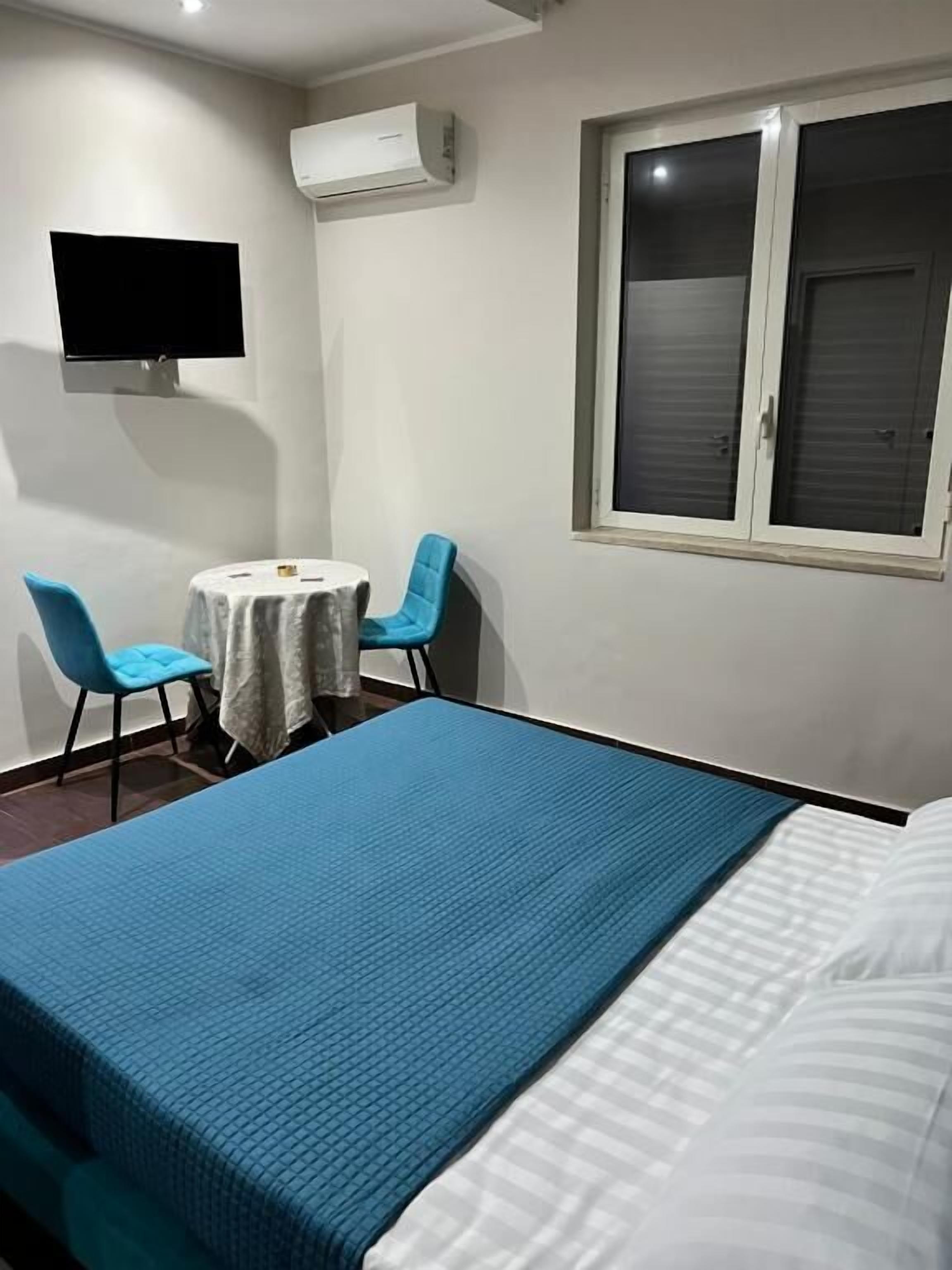 Un dormitorio con cama, una mesita, dos sillas, televisor y aire acondicionado.