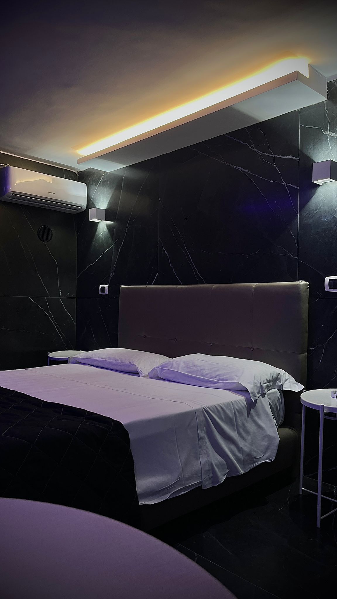 Una habitación de hotel moderna con una cama grande, una pequeña mesa redonda y un aire acondicionado instalado en la pared.
