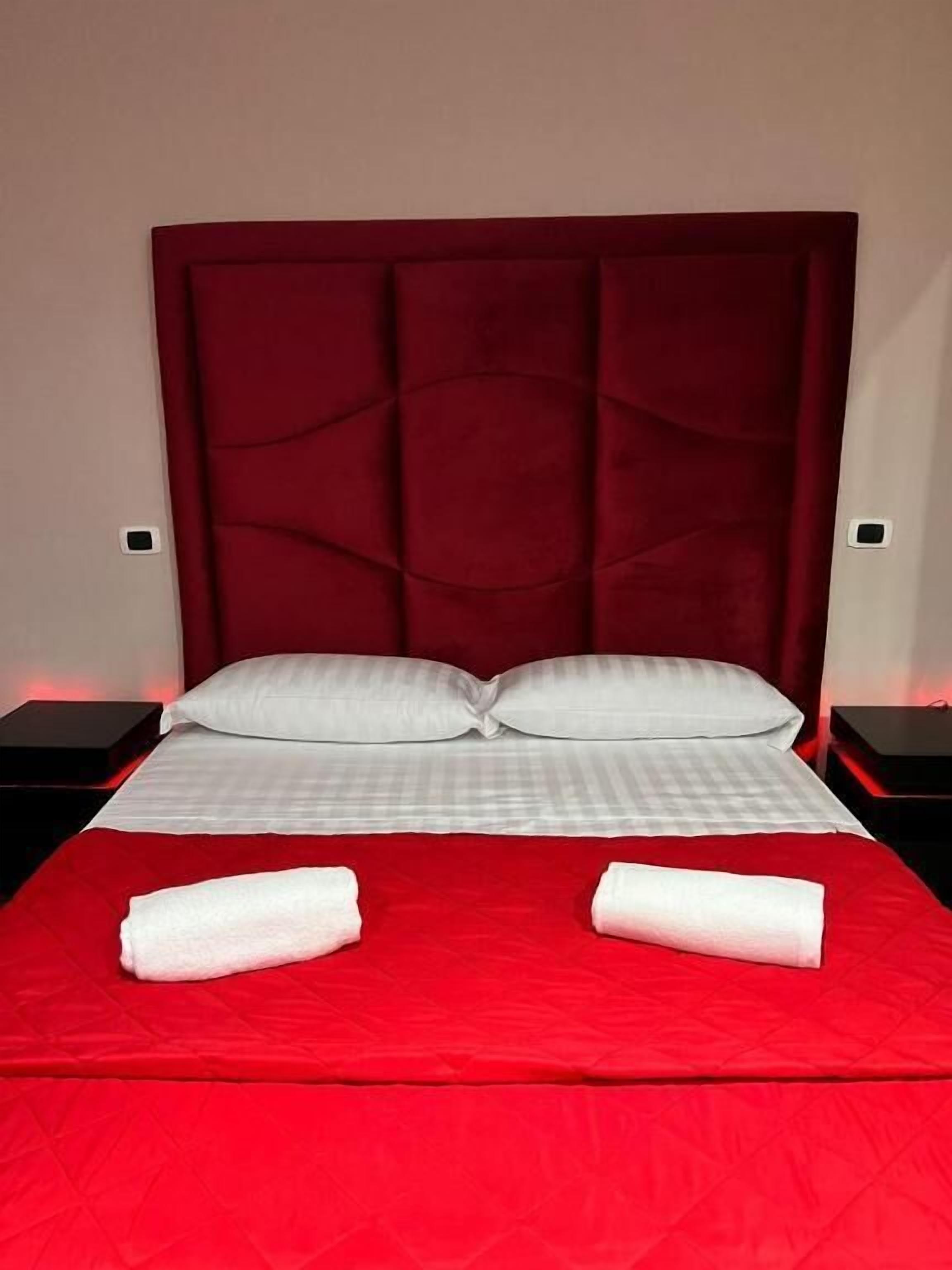A bed with a red headboard, white pillows, and two white towels on a red bedspread.
