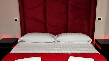 A bed with a red headboard, white pillows, and two white towels on a red bedspread.