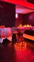 Una habitación con piso de mármol oscuro, un sofá, una mesa con mantel estampado y un oso de peluche.