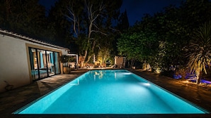 A rectangular swimming pool with a tiled deck, surrounded by trees and a building with glass doors. - Mas en Provence (Eyguières)