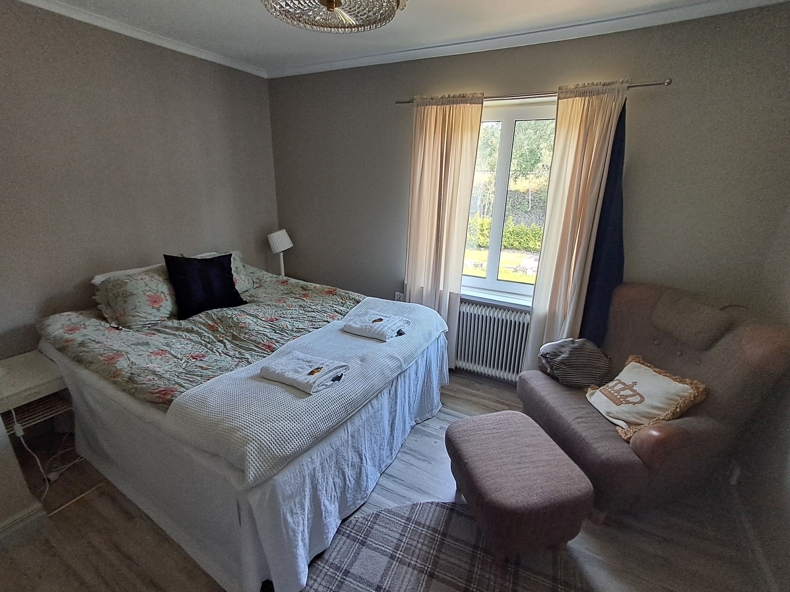 Une chambre à coucher avec un lit, une chaise, une fenêtre avec des rideaux et un radiateur.