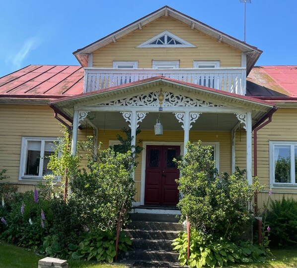 A two-story house with a porch, a red door, and a small garden with various plants.