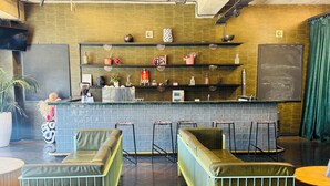 Um espaço de bar com banquetas, balcão e prateleiras com objetos decorativos.