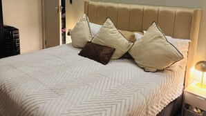 Uma cama com cabeceira acolchoada, várias almofadas, uma luminária de cabeceira e uma porta para um armário.