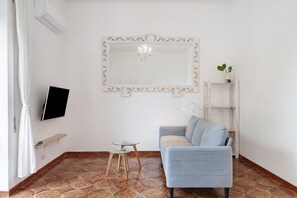A living room with a sofa, a TV, a small table, a mirror, and a plant.