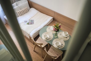 Ein ordentlich gemachtes Bett mit Kissen und einer Zeitschrift, ein kleiner Esstisch mit Tellern, Gläsern und einem Blumenstrauß.