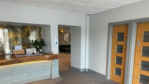 A reception area with a wooden reception desk, a sign indicating registration requirements, a potted plant, and a wall-mounted security camera. - 24 The Salcombe (Salcombe)