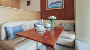 A dining area with a wooden table, white sofa, and a painting of a boat on the wall. - 24 The Salcombe (Salcombe)
