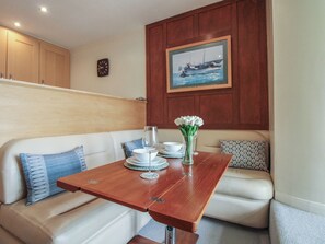 A dining area with a wooden table, white sofa, and a painting of a boat on the wall. - 24 The Salcombe (Salcombe)
