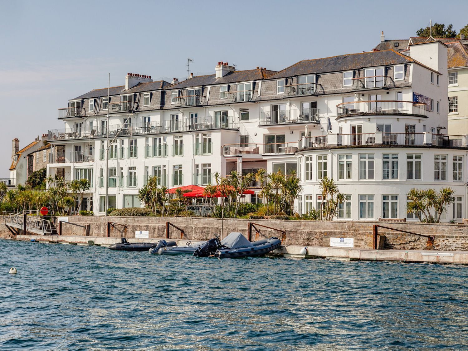 Un edifici de diverses plantes amb balcons, una vista al mar i un paraigua vermell.