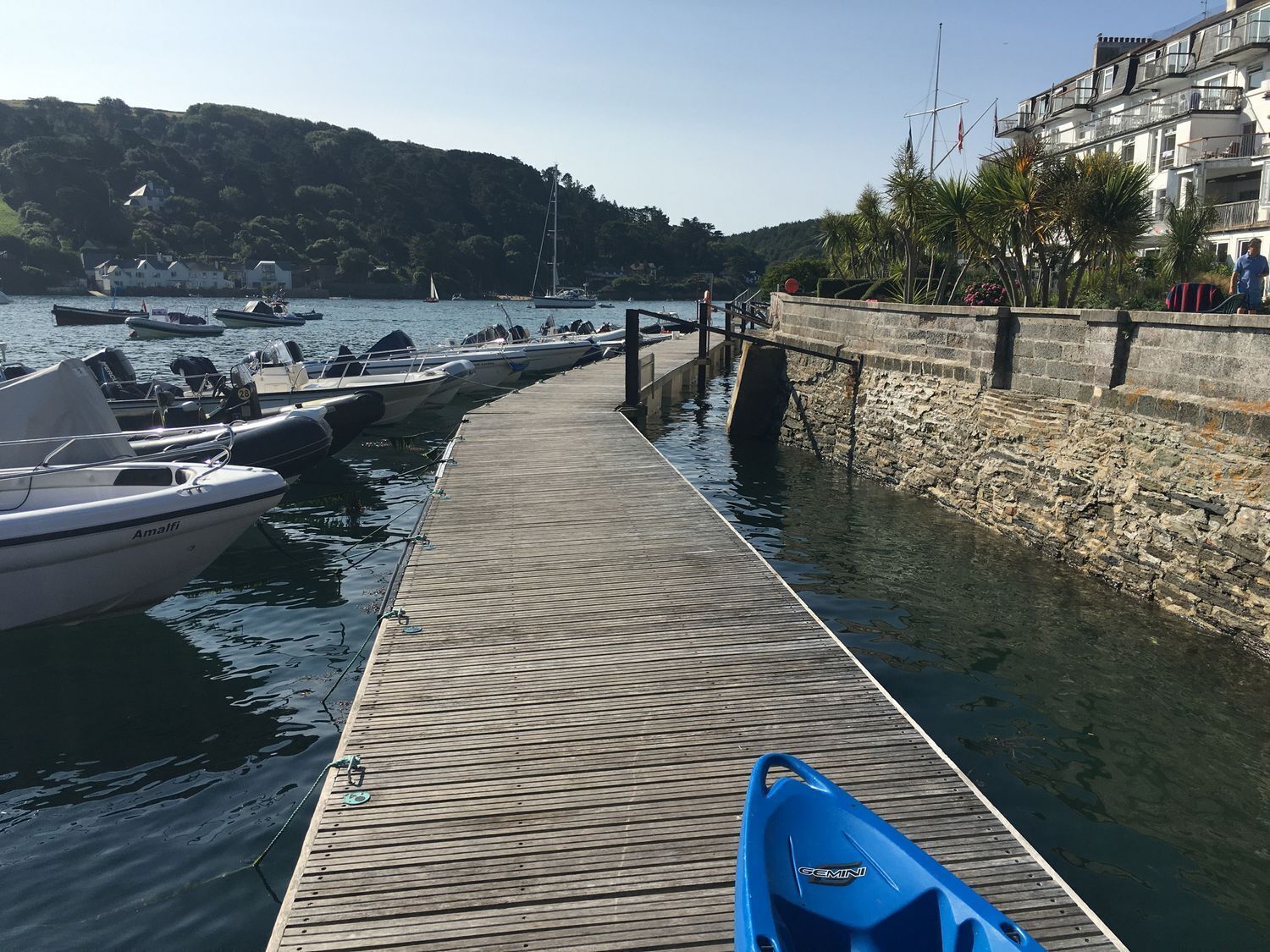Un muelle de madera que lleva a un puerto deportivo con barcos amarrados a la izquierda.