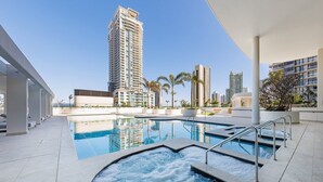 A swimming pool with a hot tub, surrounded by modern buildings and palm trees. - Lvl50 Ocean Views | 3BR Skyhome | Pool+Gym+Parking (Surfers Paradise)