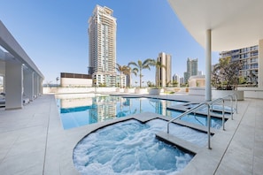 A swimming pool with a hot tub, surrounded by modern buildings and palm trees. - Lvl50 Ocean Views | 3BR Skyhome | Pool+Gym+Parking (Surfers Paradise)