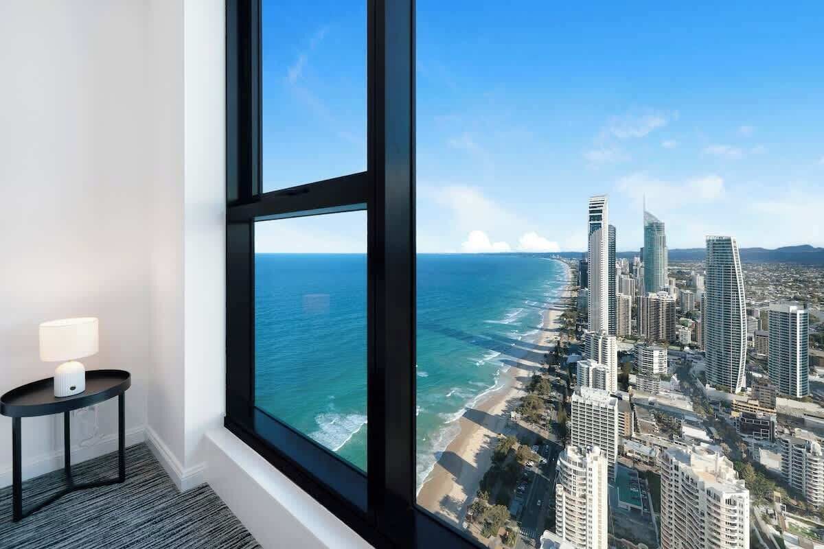 Una habitación con un amplio ventanal que da a una playa y al horizonte urbano.